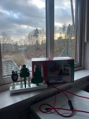 Elektrisk adventsljusstake med uggla - Elektrisk adventsljusstake i trä från Konstsmide med vit bas, gröna träd och en svart uggla. Ljusstaken har fyra ljus och röd sladd. Perfekt som juldekoration i fönstret. Passar perfekt in i ett barn rum 