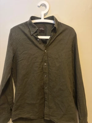 Mörkgrön linneskjorta Oscar Jacobson - Snygg mörkgrön skjorta från Oscar Jacobson i linnematerial. Skjortan har slim passform, långa ärmar och klassisk knappstängning framtill. Perfekt för dig som gillar stilrena och bekväma plagg.