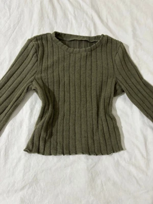 Olivgrön ribbad stickad tröja - Olivgrön ribbstickad tröja med utsvängda ärmar och rund hals som är i väldigt mjukt material. Snygg passform och coola detaljer som ger en unik look. Är i storlek s och aldrig använd. 💐🫶🏼