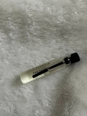 FRESHOT parfymprov i glasflaska - Liten parfymflaska från FRESHOT i genomskinligt glas med svart skruvkork. Flaskan är cylinderformad och innehåller en ljusgul vätska. Perfekt att ha med i väskan för en fräsch doft när du är på språng. Essnce