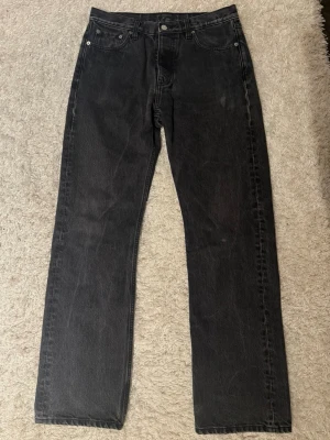 HOPE Jeans svarta - Säljer ett par svarta/gråa jeans med rak passform och klassisk femficksdesign. Jeansen har normal midja och stängs med knapp och dragkedja. Materialet är kraftig denim i bomull och färgen är tvättad svart för en cool vintagekänsla. Jeansen är i modellen ”Rush”. Ena bakfickan har en blekning, utöver det är den i gott skick.
