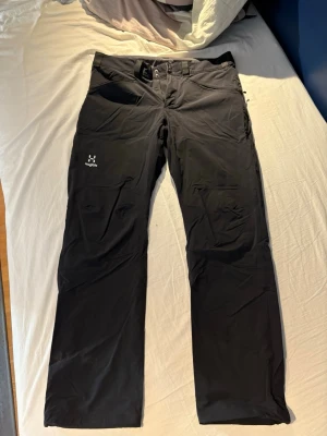 Svarta friluftsbyxor från Haglöfs - Svarta friluftsbyxor från Haglöfs med raka ben och dragkedjeförsedda fickor framtill. Byxorna har bälteshällor och är tillverkade i ett slitstarkt, stretchigt material som passar perfekt för utomhusaktiviteter. Klassisk design med diskret logga på låret.