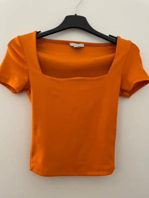 Orange croppad topp från Amisu - Snygg orange croppad topp från Amisu med fyrkantig urringning och korta ärmar. Perfekt för dig som vill ha en enkel men färgstark topp till din outfit. Tillverkad i mjuk bomull som känns skön mot huden.