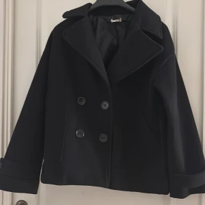 Kappa  - As snygg svart kappa från design by si. Använd några få gånger men ser helt ny ut. Nypris ca 750kr. 