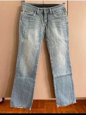 Ljusblå bootcut jeans  - Ljusblå jeans  med slitna detaljer framtill. Klassisk femficksmodell med gult broderi på bakfickorna och knappgylf. Tillverkade i denim med en lätt tvättad look.