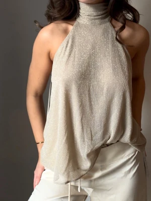 Glittrig halterneck topp från Zara - Glittrig/beige halterneck med öppen rygg. Kan knytas/stylas på olika sätt. Helt oanvänd, lappen kvar. Väldigt fin till fest eller middag.🤍