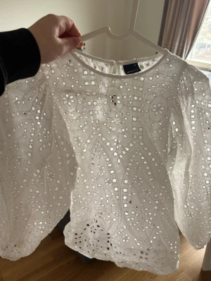 Vit broderad blus från Gina Tricot - Superfin vit blus från Gina Tricot med broderade detaljer och hålmönster. Blusen har rund halsringning och vida långärmade ärmar. Tillverkad i ett lätt och luftigt bomullstyg som ger en romantisk vibe.