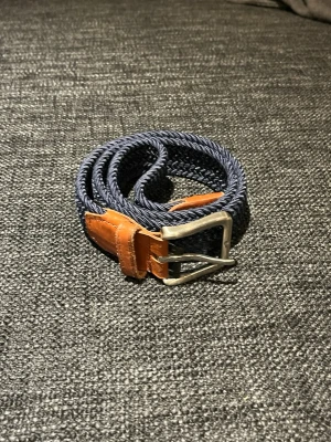 Flätat bälte från Jack & Jones - Snyggt blått flätat bälte med bruna skinn-detaljer och silvrigt spänne från Jack & Jones. Perfekt accessoar för att lyfta din outfit med en klassisk touch. Bältet har en flexibel design och passar till många olika stilar. Storlek 90 och har en liten skavank som knappt är synlig.