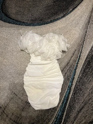 Vit axelbandslös kortklänning med volang - Helt ny superfin vit axelbandslös kortklänning med stora volangdetaljer upptill. Klänningen har en tight passform och är perfekt för dig som vill sticka ut. Materialet känns slätt och har en lätt glans. Perfekt för speciella tillfällen när du vill känna dig extra glam.