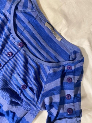 Jättecool randning t-shirt med knappar - In Wear t-shirt med superfina knapp-detaljer. Fin modell som sitter skönt. Passar bra på mig och jag har typ S men beror på hur man vill att den ska sitta. Knapparna och ränderna gör tröjan så unik💕