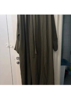 Olivgrön lång morgonrock med skärp - Mysig olivgrön morgonrock i lång modell med vida ärmar och tillhörande midjeskärp. Perfekt för att chilla hemma och svepa in sig i efter duschen. Materialet excluerar en mjuk och avslappnad känsla. Inga synliga detaljer eller mönster.