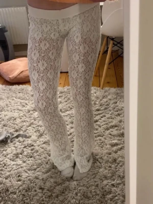 Vita spetsleggings med utsvängda ben - Säljer ett par vita leggings i spets med utsvängda ben. De har ett snyggt blommigt spetsmönster och bred resår i midjan. Perfekta för dig som vill sticka ut med en trendig och unik look.
