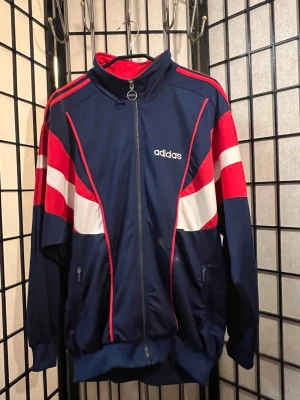 🔥 Adidas Vintage Track Jacket – Y2K Sportcore – Navy/Röd – L -  Riktig early 2000s adidas track jacket i clean navy med röda & vita paneler. Exakt den typen av zip som funkar till baggy jeans, parachute pants eller jorts.  Stor metall-ringzip med adidas-logo Broderad adidas bak i kragen Fett färgblock som ger riktig 00s Euro sport vibe Skön oversized passform (märkt F180 – sitter som L)  Perfekt för: y2k blokecore mcbling era retro sport football core festival fits  Skick: Mycket bra vintage-skick. Inga hål eller större defekter.  Mått skickas vid behov. 