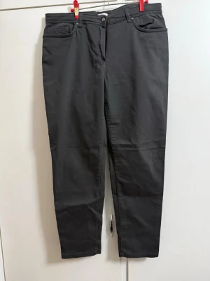 Svarta raka jeans med nitar från ANTONELLE - Säljer ett par svarta jeans med rak passform och klassisk femficksdesign. Jeansen har nitar som detalj på bakfickorna och bälteshällor i midjan. Materialet är mjukt och stretchigt för extra komfort. Perfekta för en stilren och enkel look.