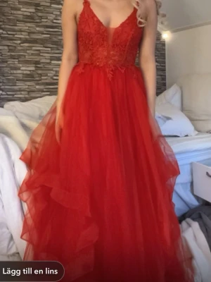 Röd långklänning med spets och volang - Säljer en röd långklänning med spetsdetaljer upptill och volangig kjol i flera lager. Klänningen har smala axelband, v-ringning och en romantisk look. Perfekt för bal eller festliga tillfällen. Materialet känns lätt och luftigt.