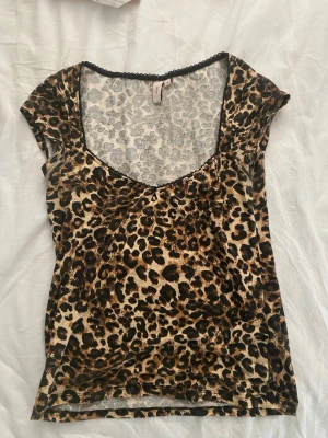 Leopardmönstrad topp med v-ringning - Snygg leopardmönstrad topp från Nelly med v-ringning och korta ärmar. Tunn och stretchig i materialet, perfekt för att sticka ut. Svart spetsdetalj vid halsringningen ger en extra touch.