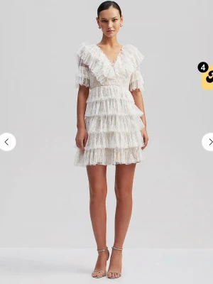 By Malina Vit spetsklänning med volanger - Säljer en by malina klänning i XS, använd 1 gång, perfekt till student eller skolavslutning! En kort vit klänning med flera lager volanger och spetsdetaljer. Klänningen har v-ringning, korta ärmar och öppen rygg. Perfekt för dig som gillar romantisk och feminin stil. Passformen är normal och materialet är spets.