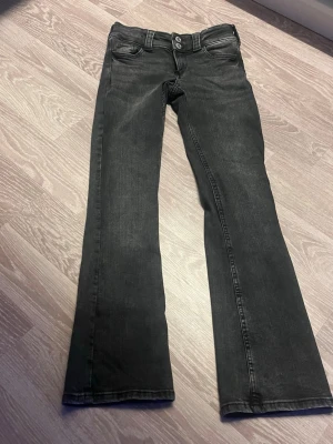Svarta bootcut jeans med dubbla knappar - Snygga svarta bootcut jeans med dubbla knappar i midjan och klassiska fem fickor. Jeansen har lätt utsvängda ben och silverfärgade detaljer på bakfickorna. Perfekta för en trendig och avslappnad stil.