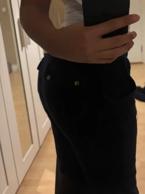 Mörkblå juicy byxor perfekt kondition - Säljer ett par mörkblå byxor raka ben och snygga guldknappar på fickorna. Byxorna har hög midja och klassisk femficksdesign. Perfekta för dig som vill ha en stilren och trendig look med retrovibbar.