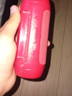 Röd trådlös högtalare cylinderformad - Snygg röd trådlös högtalare med cylinderformad design. Högtalaren har knappar på sidan för enkel styrning och ett nätgaller som skyddar högtalarelementen. Perfekt för att ta med sig överallt och spela musik trådlöst via Bluetooth.