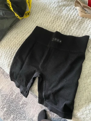 Svarta ribbade cykelshorts YOOA - Svarta cykelshorts från YOOA med ribbad struktur och hög midja. Stretchigt material som sitter skönt och följsamt. Perfekta för en sportig look eller till oversized t-shirt. Kort modell som slutar mitt på låret.
