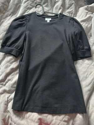 Svart topp med puffärm från Vero Moda  - Stilren svart topp från Vero Moda med puffärmar och rund halsringning. Mjukt material som känns skönt mot huden. Perfekt för dig som vill ha en enkel men trendig look med lite extra volym på ärmarna.