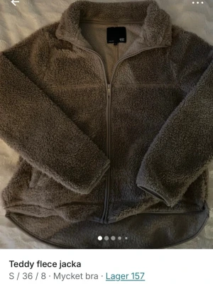 Brun teddyjacka från Lager 157 - Mysig brun teddyjacka från Lager 157 med dragkedja framtill och hög krage. Jackan är tillverkad i mjuk teddyfleece och har en avslappnad passform med långa ärmar. Perfekt för att hålla värmen under kyliga dagar.