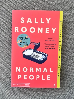 Normal People av Sally Rooney - Romanen 'Normal People' av Sally Rooney är en modern skönlitterär bok med röd och gul mjukpärm. Omslaget har en illustration av en konservburk och tydlig vit text. Boken är på engelska och handlar om relationer, vänskap och kärlek i Irland.