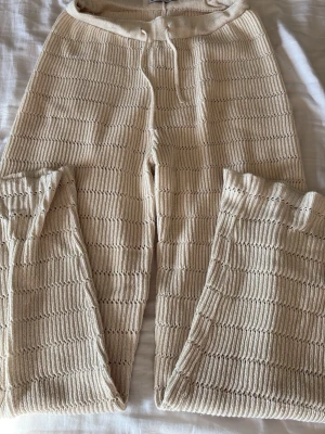Stickade beige mjukisbyxor från ONLY - Supermysiga stickade mjukisbyxor i beige från ONLY. Byxorna har ett snyggt hålmönster, resår och dragsko i midjan samt raka ben. Perfekta för chill dagar hemma eller när du vill vara extra bekväm. Materialet är mjukt och stretchigt stickat tyg.