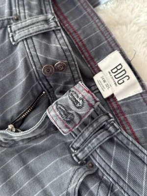 Unika Gråa bootcut jeans med ränder från BDG - PRIS KAN DISKUTERAS! ❤️🤗Snygga gråa bootcut jeans med vita vertikala ränder och låg midja. Jeansen har klassisk femficksdesign och dubbla knappar framtill. Perfekta för en trendig och avslappnad look. Från  Urban Outfitters
