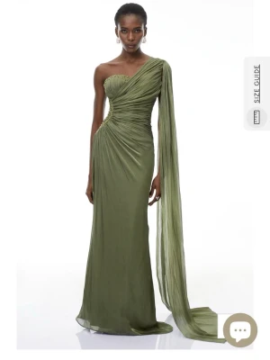 Grön långklänning med oneshoulder - Elegant grön långklänning med draperad design och oneshoulder. Klänningen har en lång, svepande ärm och vackra veck över byst och midja. Klänningen är oanvänd och säljs då paketet kom försent. Nypris är 2236 kr.