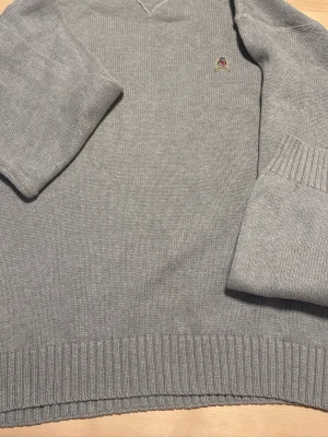 Grå stickad tröja Tommy Hilfiger - Snygg grå stickad tröja från Tommy Hilfiger i 100% bomull. Tröjan har ribbade muddar vid ärmslut och nederkant samt en liten broderad logga på bröstet. Pris kan diskuteras 
