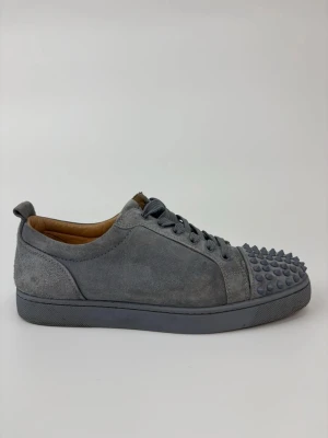 Gråa sneakers med nitar från Louboutin - Gråa sneakers i mocka från Christian Louboutin med coola runda nitar på tån. Skorna har lågt skaft, matchande grå snörning och en mjuk innersula i läder. Perfekta för dig som vill sticka ut med en edgy och lyxig stil.