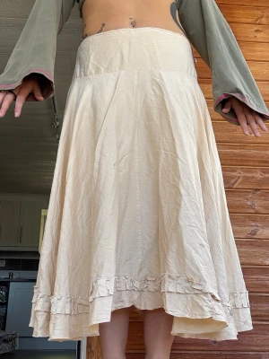 Beige långkjol med volangkant - Säljer en beige långkjol med bred midja och volangdetalj längst ner. Kjolen har en lätt utsvängd form och är tillverkad i ett tunt, mjukt material som ger ett flowy intryck. Perfekt för dig som gillar en bohemisk och avslappnad stil. Sitter såhär på mig med storlek 40/42. Har några fläckar som jag ej testat ta bort se sista bilderna. 