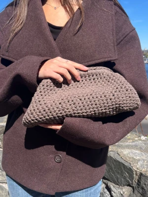 Virkad Clutch väska beigebrun - Vi är ett UF-företag som säljer handvirkade Clutchväskor! 🩷 Denna väska är i färgen beigebrun. Väskan har en unik form och känns både trendig och är handgjord. Perfekt för dig som gillar en personlig touch på din outfit! 