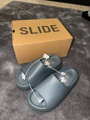 Yeezy slides - Helt nya och oanvända yeezy slides i en snygg grå färg perfekt till sommaren. Extremt mjuka och bekväma att ha på sig, som att gå på moln. Säljer dessa för de inte passade mig.