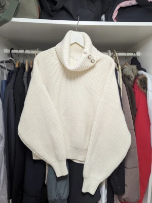 Vit stickad polotröja från H&M - Snygg vit stickad polotröja från H&M med bred ribbad krage och dekorativa pärlknappar. Tröjan har oversized passform och långa ärmar. Perfekt för lager-på-lager och en trendig look.