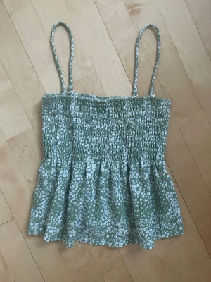 Grön blommig linnetopp - Söt grön linnetopp med vita små blommor och smala axelband. Toppen har smockad överdel och volang nedtill för en luftig och somrig känsla. Perfekt för varma dagar och enkel att matcha med jeans eller kjol. Mitt pris 130kr🌸