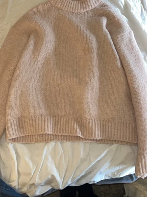 Beige stickad tröja med polokrage - Mysig beige/rosa stickad tröja med polokrage och ribbade muddar vid ärmslut och nederkant. Tröjan har en avslappnad passform och är perfekt för lager-på-lager-stil. Materialet känns mjukt och skönt mot huden.