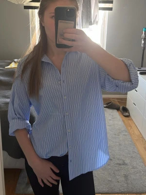 Blåvit randig skjorta - Snygg oversized skjorta i blått och vitt med tunna ränder. Skjortan har klassisk krage, knäppning framtill och långa ärmar som kan vikas upp. Aldrig använd