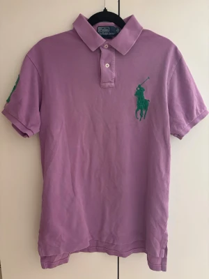 Ralph Lauren Custom Fit polo - Oanvänd Ralph Lauren pikétröja i lila med gröna detaljer. Custom Fit-modell, i nyskick.