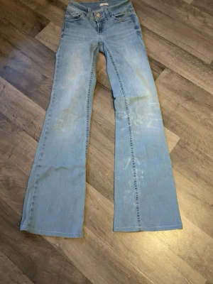 Ljusblå bootcut jeans med brodyr - Säljer ett par ljusblå bootcut jeans med snygg broderad detalj i rött på bakfickorna. Jeansen har klassisk femficksmodell och utsvängda ben. Perfekta för dig som gillar retrostil och vill ha ett par riktigt sköna jeans i mjukt denimtyg. Dom har lite vita defekter på sig som kommit från tvätten. Säljs billigt 