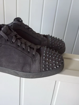 Gråa sneakers med nitar på tån - Säljer ett par gråa sneakers med coola nitar på tån. Skorna har snörning och är tillverkade i ett matt tygmaterial. Perfekta för dig som vill sticka ut med en grisch stil. Passar till streetwear och ger en unik touch till outfiten.