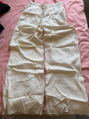 Vida beige linnebyxor från Zara - Säljer ett par ljusbeige linnebyxor med avslappnad passform och breda ben. Byxorna har resår i midjan och dragsko för extra komfort. Perfekta för en chill och stilren look. Materialet är luftigt och svalt linne. Använda en gång!