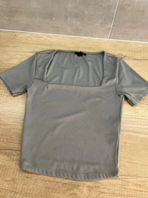 Grå topp med fyrkantig ringning Amisu - Snygg grå topp från Amisu med korta ärmar och fyrkantig ringning. Tillverkad i ett mjukt och stretchigt material som känns skönt mot huden. Perfekt att styla med jeans eller kjol för en clean look.
