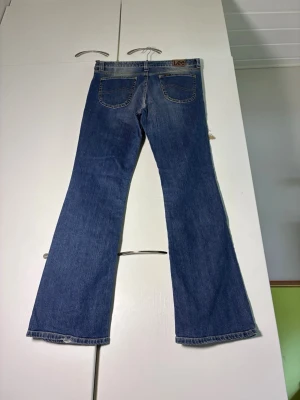 Blå flare jeans från Lee - Snygga blå flare jeans från Lee med klassisk femficksdesign och ljusa slitningar framtill. Jeansen har normalhög midja och är tillverkade i denim med tydliga kontrastsömmar. Perfekta för en avslappnad och trendig look.