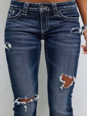 Mörkblå slitna bootcut jeans - Mörkblå bootcut jeans med slitningar och hål på låren och knäna. Jeansen har vit kontrastsöm, klassisk femficksmodell och låg midja. Perfekta för en avslappnad och trendig look.