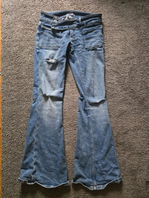 Gina young S14+ Nya! utsvängda jeans med slitningar - Säljer ett par blå jeans med utsvängda ben och coola slitningar på låret. Jeansen har klassiska fickor fram och bak samt låg midja och bootcut.  Dom är helt nya , köpta till min dotter i mars , hon använde dom nån gång men kände sen att dom inte satt som hon ville. 