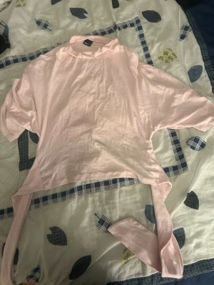 Ljusrosa crop top med knytband  - Säljer en ljusrosa crop top med vida ärmar och långa knytband i midjan. Toppen har en lös passform och är gjord i ett mjukt, tunt tyg som känns skönt mot huden. Perfekt att styla med höga jeans eller kjol för en trendig look.
