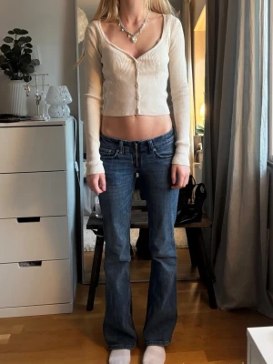 Snygg vit ribbad kofta! - Säljer en vit, ribbad och croppad topp med lång ärm och v-ringning. Toppen har knäppning framtill med små knappar och är figurnära i modellen. Perfekt för dig som gillar en enkel men trendig stil.